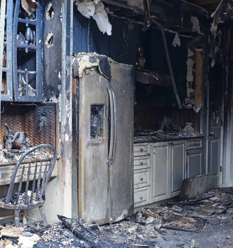 Charred kitchen with appliances, cabinets, and countertops showing extensive fire restoration damage.