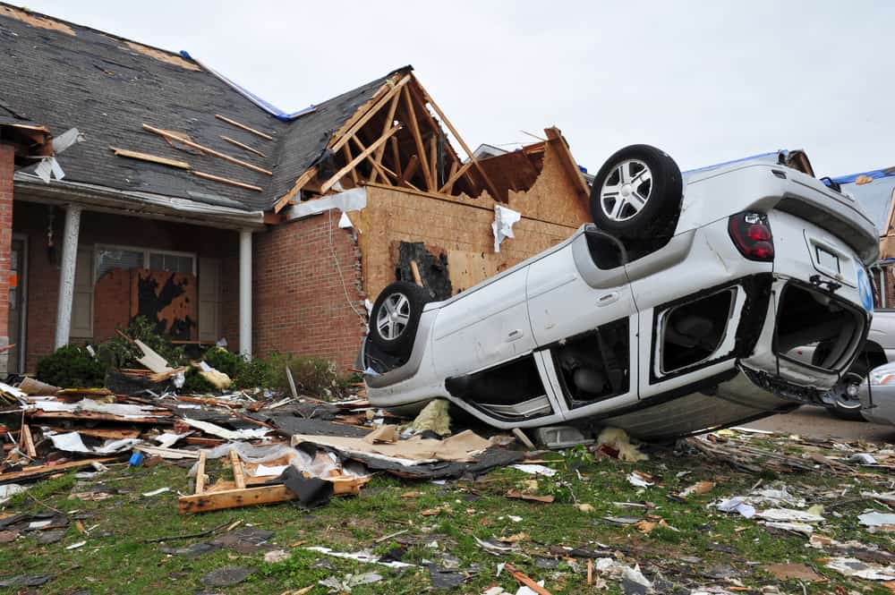 Destroyed house with debris scattered, and a flipped-over car, illustrating the aftermath of natural disaster restoration.