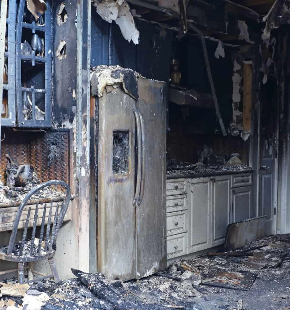 Charred kitchen with appliances, cabinets, and countertops showing extensive fire restoration damage.