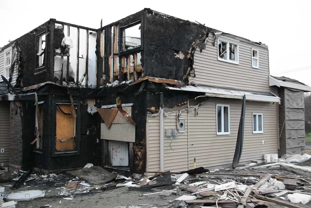 House exterior with charred remnants, displaying extensive fire restoration damage.